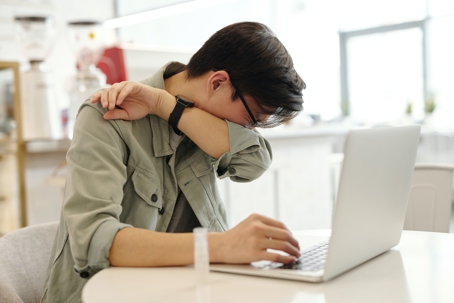 Man using a laptop sneezing on his arm sleeves